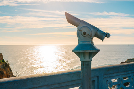 Metal viewing telescope overlooks the ocean with sunlight reflecting off the water under a serene sky.の写真素材