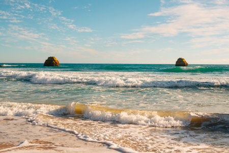 Waves rolling in towards the beach with serene ocean rocks on the horizon.の写真素材
