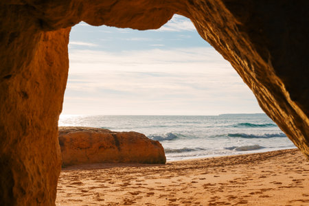 Rolling waves break gently on the sandy shore, with two isolated rock formations rising from the turquoise ocean under a sunny sky.の写真素材