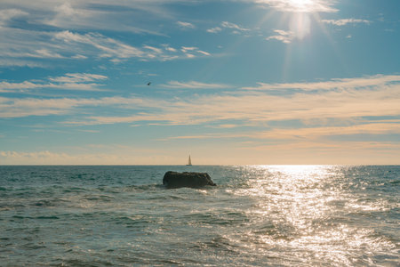 Gentle waves crash onto the sandy shore as rocky outcrops rise from the turquoise ocean under a clear sky.の写真素材