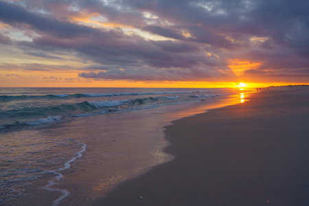 Sunset bursts through the clouds, casting vibrant colors over the ocean and beachの写真素材
