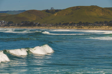 Ocean waves crest and roll in front of a scenic hillside village.の写真素材