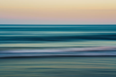 Blurred ocean waves meet a pastel sky at sunset.の写真素材