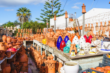 Outdoor display of terracotta pottery and colorful ceramic ornaments under a bright blue sky.の写真素材