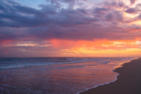 Intense sunset colors of red, purple, and orange fill the sky and reflect on the shoreline.の写真素材