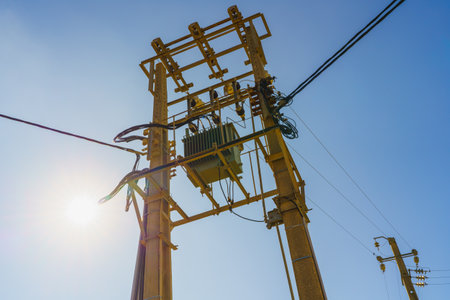 Electrical power transformer mounted on a utility pole with wires against a clear blue sky.の写真素材
