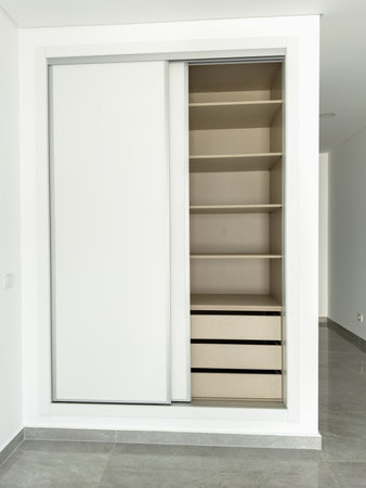 Modern built-in wardrobe with white sliding doors, open to reveal shelves and drawers.の写真素材