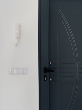 Sleek metal door with decorative patterns beside a wall-mounted intercom and light switches.の写真素材
