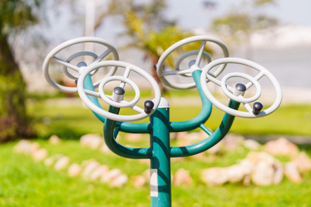 Stationary exercise equipment with a green metal frame and white wheels is installed in a public park.の写真素材