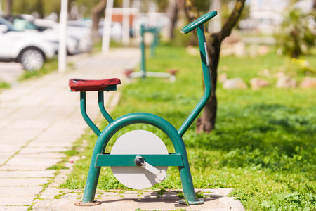 Outdoor stationary exercise bike with a green metal frame and red seat is installed in a public park.の写真素材