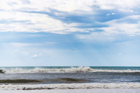 Serene ocean waves roll in under a partly cloudy blue sky.の写真素材