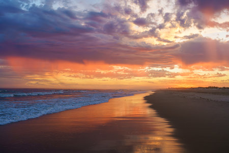 Vibrant sunset colors reflect on the shoreline as waves gently roll in.の写真素材