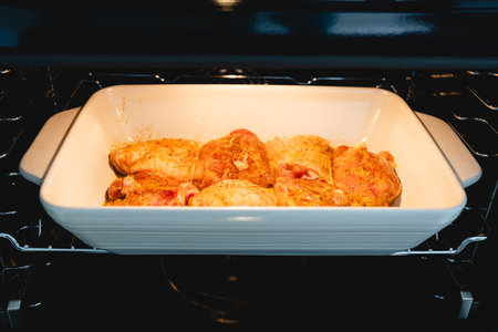 Spiced chicken thighs begin roasting in the oven inside a ceramic baking dish.の写真素材