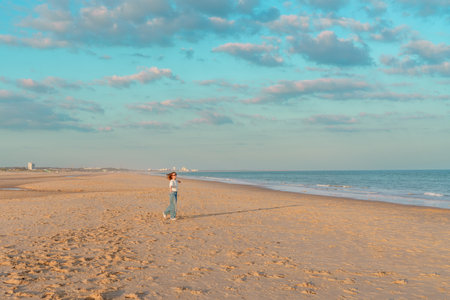 Woman in white shirt and jeans standing alone on the beach looking at the ocean, enjoying the moment.の写真素材