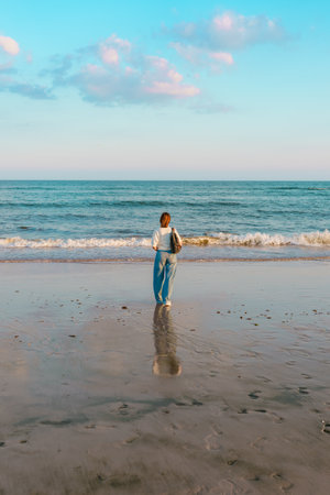 Woman facing the ocean, standing at the water's edge with her reflection visible on the wet sand.の写真素材
