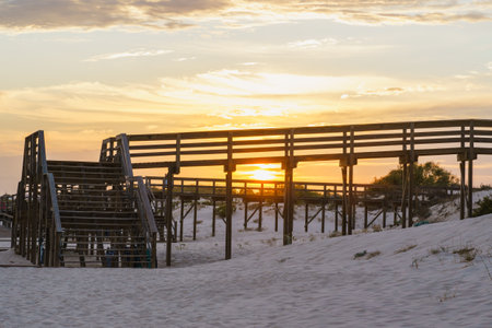 Sunset shining through a wooden boardwalk on a sandy beach.の写真素材