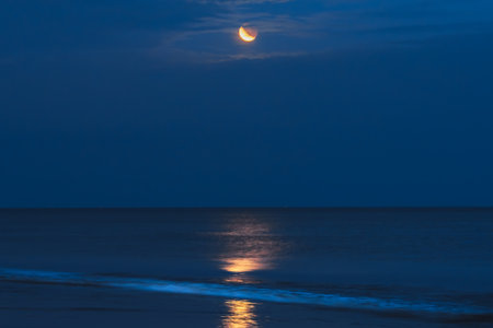A crescent moon casts a golden reflection across the still water under a deep blue night sky.の写真素材