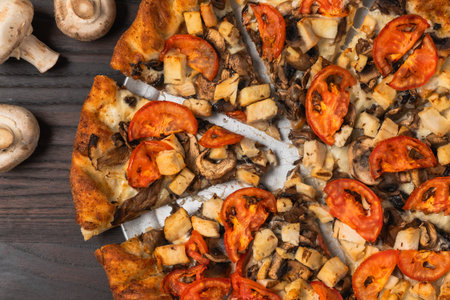 Wood-fired pizza topped with mushrooms and sliced tomatoes on a golden crust.の写真素材