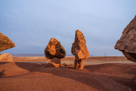 Two uniquely shaped rock pillars stand upright on red desert ground under a soft blue sky.の写真素材