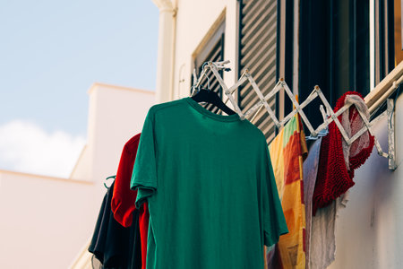 Brightly colored clothing and towels hang from an extended drying rack on a residential balcony.の写真素材