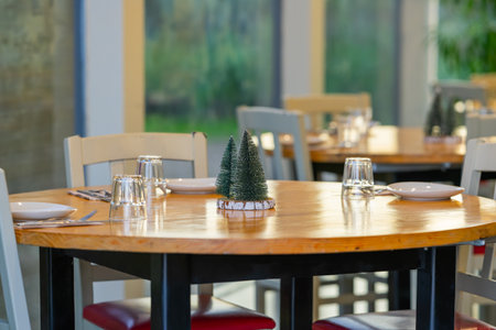 Round wooden table set with plates and glasses, decorated with small artificial pine trees