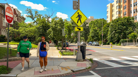 Washington D.C. USA - May 24, 2025. Pedestrians walk under bright signage near a leafy intersection.
