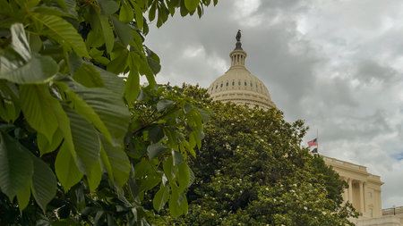 Washington D.C, USA, May 22, 2025. The U.S. Capitol stands in the distance behind a lush green lawn and trees, beneath a partly cloudy spring sky.のeditorial素材