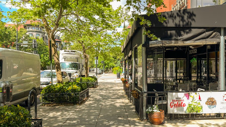 Washington D.C. USA - May 24, 2025. A shaded cafÃ© patio sits next to parked delivery trucks and lush city trees.のeditorial素材