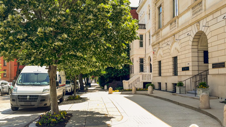 Washington D.C. USA - May 24, 2025. Trees line a clean sidewalk beside elegant stone buildings and...