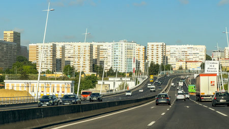 Lisbon, Portugal, May 20, 2025. A busy multilane highway curves toward high-rise residential buildings as vehicles pass beneath overhead cables marked with red warning spheres.のeditorial素材