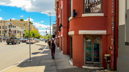 Washington D.C., May 24, 2025. A pedestrian carrying bags strolls past red-brick buildings near a busy intersection.のeditorial素材