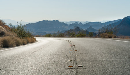 A desert highway leads toward distant jagged mountains under a hazy sky.