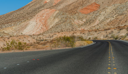A blacktop road snakes through a desert landscape marked by multicolored rock formations.の写真素材