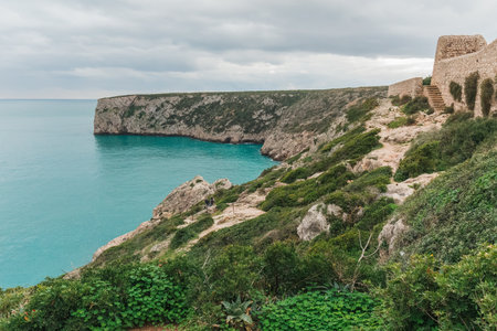 A rugged coastal path winds past ancient stone walls overlooking a calm turquoise bay.の写真素材