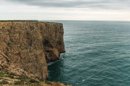 Steep vertical rock wall meets the calm sea under a soft overcast sky.の写真素材