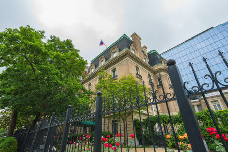 Washington D.C., USA - May 21, 2025.  Ornate embassy building with a flag, manicured garden, and wrought-iron fence.のeditorial素材