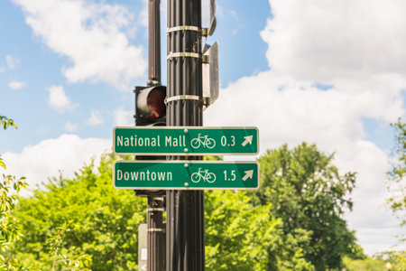 Washington D. C., USA - May 24, 2025. A green bike route sign shows directions to National Mall and Downtown with distances.