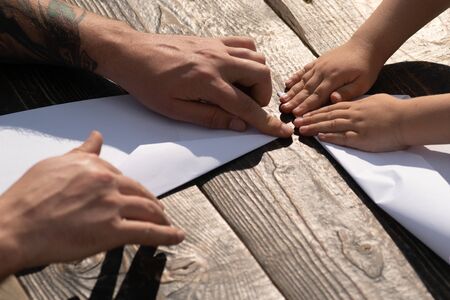 Family time. Father and son make a paper airplane. Summer holidays. Time together. Family hobby. Father teaches son origami. Master class from dad. Hands of a child and an adult. Love, fathers day.の写真素材