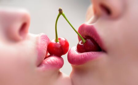 Sweet kiss. Lesbian couple. Female lovers enjoying erotic act with red cherries. Two young girls...