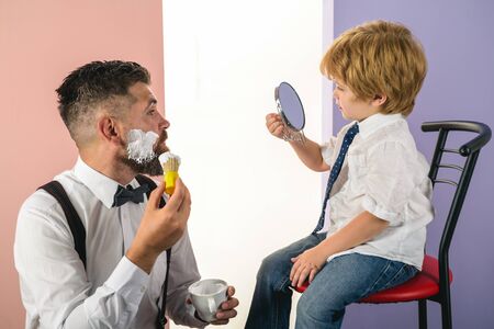 Barbershop. Trendy and stylish father and son. Barber shaving a bearded man in a barber shop. Barber Shop Studios. Professional hairstylist. Hairdressers work.の写真素材