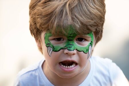 Dragon body art. Child with a mask on his face. Carnival. Favorite hero for a childrens party. Green face and fangs. A game. Fun for kids. Childrens theater. Kindergarten and party for preschoolers.の写真素材