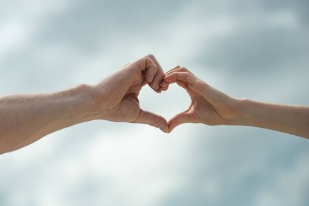 Heart sign. Hands show a heart symbol on sky background. Love. Man and woman. Partnership. Gender...