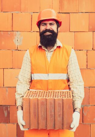 Man with brick on orange wall construction background. Construction builder worker at building site.の写真素材
