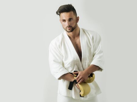 Young man wearing boxing gloves for box and combat sports. Portrait of sportsman in a white kimono...