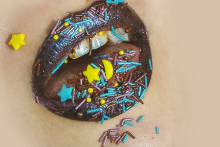Brown lips in sweets star. Colorful sprinkles on lips, teeth and in mouth. Close up lips and teeth. Sweet makeup for Easter. Brown trendy lipstick on lips. Brith blue lip gloss on brown lipstick.の写真素材