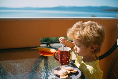 Breakfast. The boy eats porridge for children. A child sits on a terrace on a warm day. Food.の写真素材