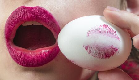 Easter egg concept. Lipstick print on round egg. Female mouth and red fashionable lipstick. Beautiful symbol of femininity life. Woman or girl holding an egg and kiss. Cosmetics for housewife. Food.の写真素材