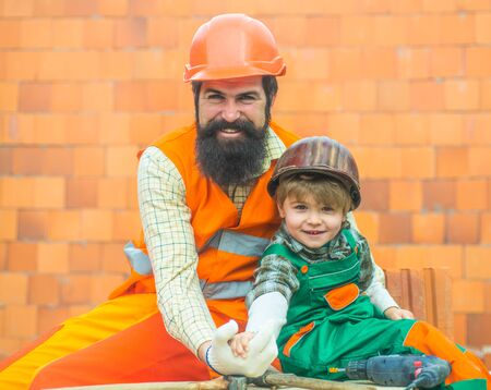Build. Successful team. Father and son at a construction site. Profession. A boy in a suit of a builder and his bearded foreman.の写真素材