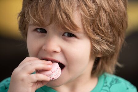 Cute child eats macaroon. Portrait with sweets. Calories and dessert. Tasty biscuit cookie. Young kid having a snack breaks with delicacy macaroon. Pastry pink macaroon.の写真素材