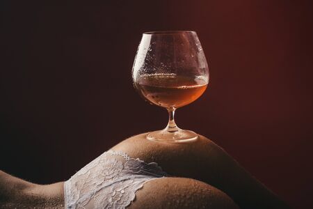 Cognac on the naked female ass. A glass of alcohol. Sexy evening. Alcohol before sex. Stress and...